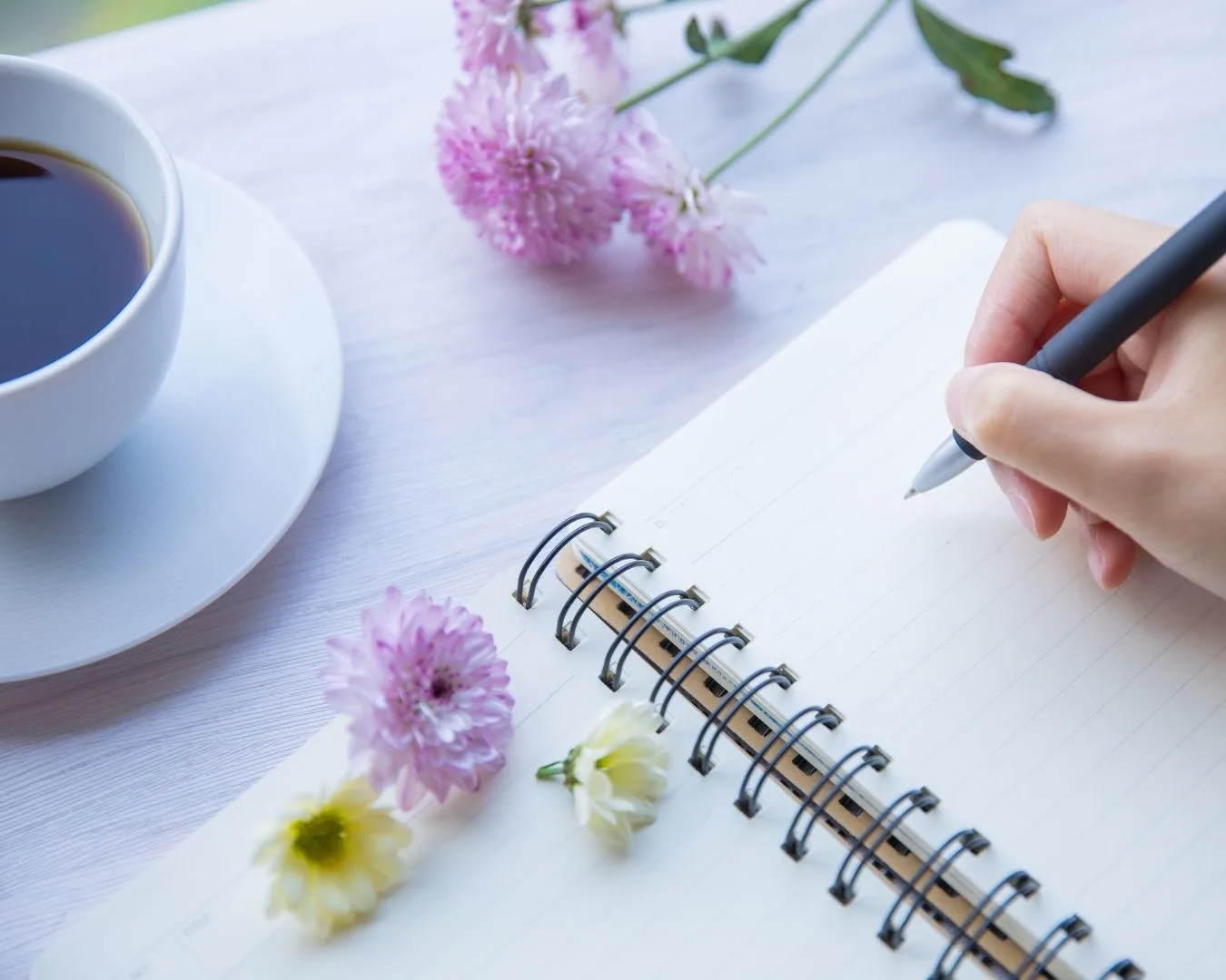 Mano femenina escribiendo en un cuaderno con luz natural, símbolo de organización, calma y acompañamiento práctico — recursos y guías para madres de niños neurodivergentes.