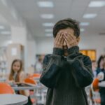 Niño cubriéndose la cara en una sala de clases bulliciosa: por qué el procesamiento sensorial de tu hijo es real, no un capricho.